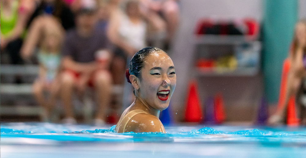 Artistic swimmer smiles in the pool after finishing her routine.